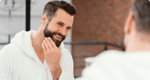 Vyriškas botoksas: atvirai apie tai, ko tikėtis žilstelėjęs vyras žiūri į veidrodį ir šypsosi