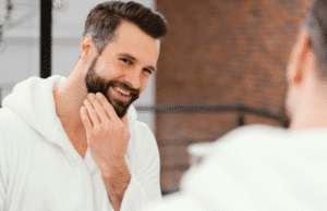 Vyriškas botoksas: atvirai apie tai, ko tikėtis žilstelėjęs vyras žiūri į veidrodį ir šypsosi