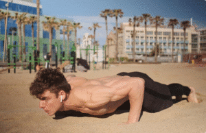 7 fitneso mitai, kuriais vis dar tikite (ir kurie tyliai griauna jūsų pastangas) jaunas vyras paplūdimyje daro atsispaudimus