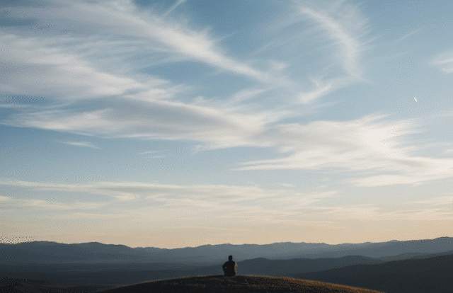 vyras sėdi ant kalno dangaus fone