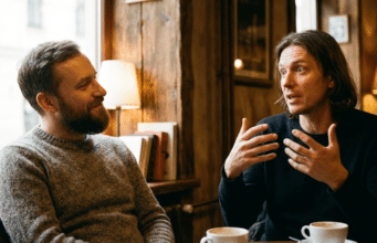 Veidrodžio principas: kaip paprastas atkartojimas padeda užmegzti ryšį? du vyrai kalbasi kavinėje, vienas gestikuliuoja ir pasakoja kitam